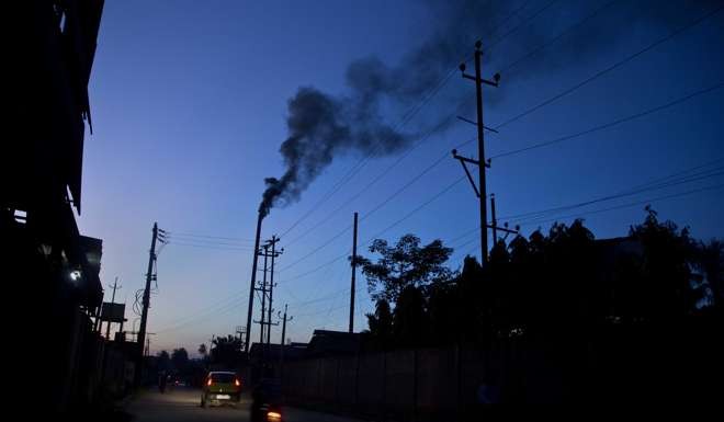 Traffic moves as smoke emits from the chimney of a factory on the outskirts of Gauhati, India. Photo: AP