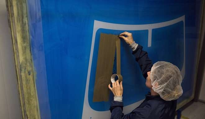 An employee uses tape to mask off an area where auto glass will be painted at the Fuyao Glass America production facility . Photo: Bloomberg
