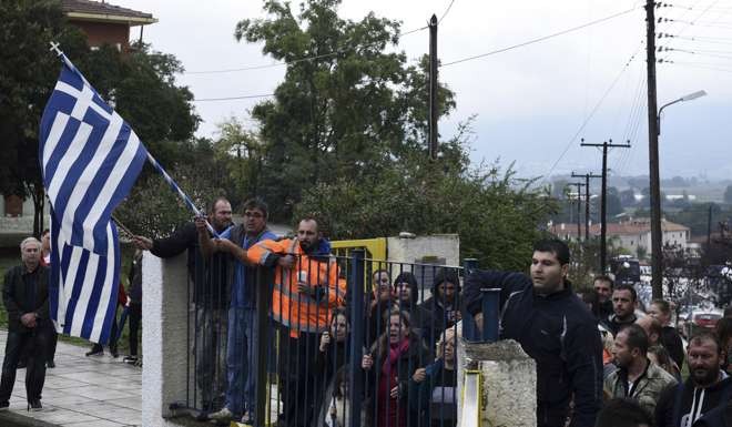 Local residents hold Greek flags during a protest outside a school at the Greek village of Profitis, east of Thessaloniki, as they attempted to block access to a primary school where children from a nearby refugee camp were due to start lessons on Monday. Photo: AP