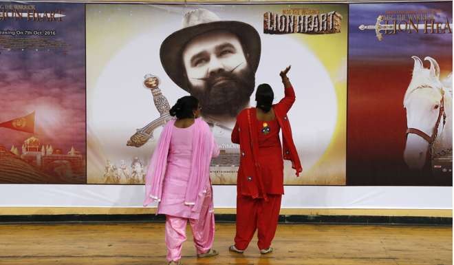 Devotees of Indian spiritual guru Saint Dr. Gurmeet Ram Rahim Singh Ji Insan stand near a poster of his new film MSG, The Warrior Lion Heart, in New Delhi. Photo: AP