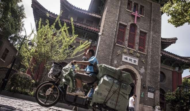 A deliveryman rides past a Catholic church in Shanghai. Photo: AFP