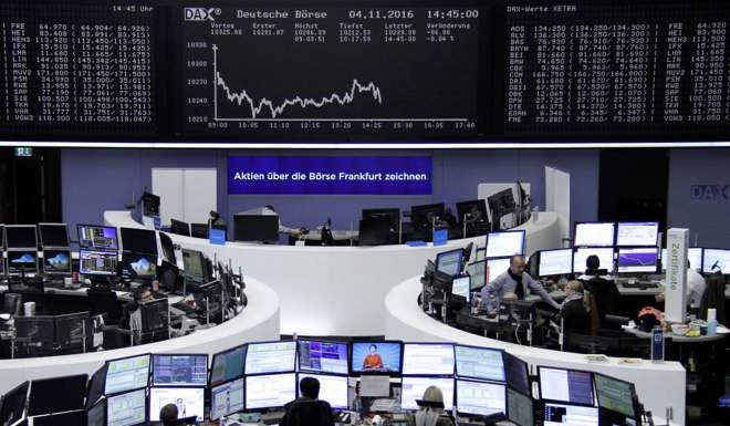 Traders work at their desks in front of the German share price index, DAX board, at the stock exchange in Frankfurt, Germany. Photo: Reuters