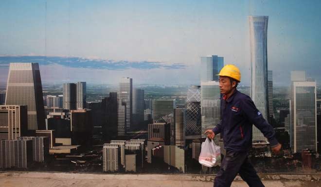 A worker walks past a poster placed outside a construction site in Beijing. Housing activities benefit construction, upstream materials suppliers and downstream real estate services. Photo: EPA