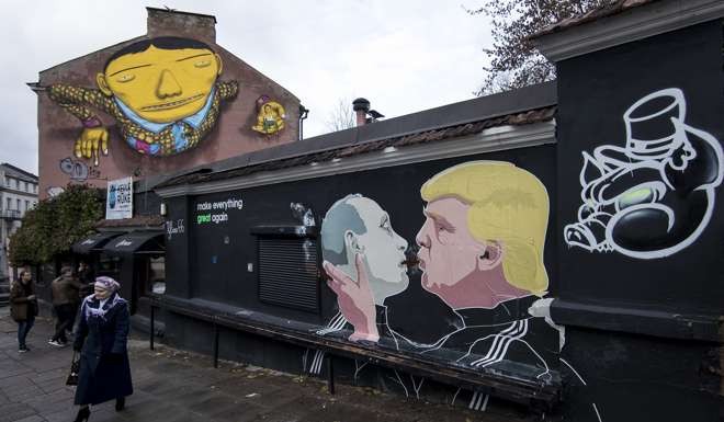 A woman walks past a graffiti artwork depicting Russian President Vladimir Putin US President-elect Donald Trump kissing, in Vilnius, Lithuania. Photo: AP
