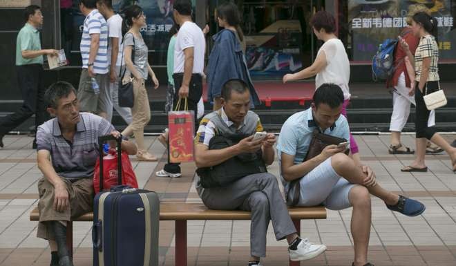 People use their smartphones while sitting on a bench at a shopping district of Beijing. Photo: EPA