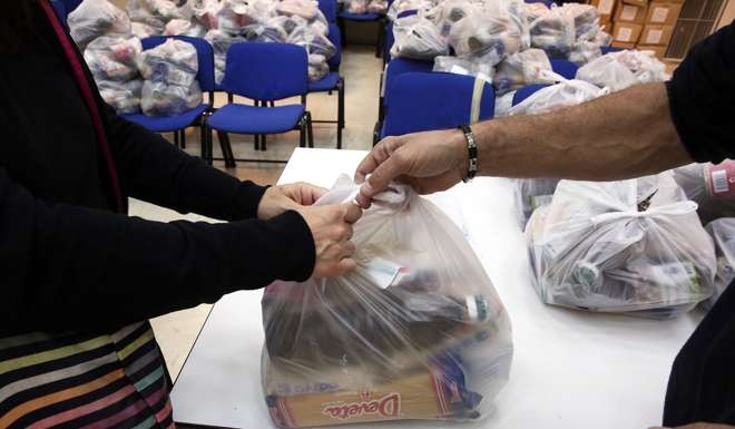An employee (R) of the Municipality of Athens hands over bags with supplies to a poor resident of the city, Photo: EPA