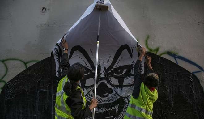 Government workers remove a street art poster depicting Najib as a clown. Photo: EPA