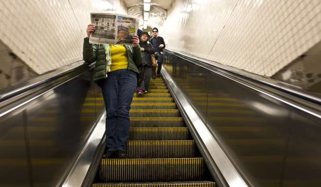 A woman reads a newspaper featuring Donald Trump while going down an escalator at a subway station in New York. Today, having elected Trump to be their next president, Americans confront a new Catch-22. Photo: AP