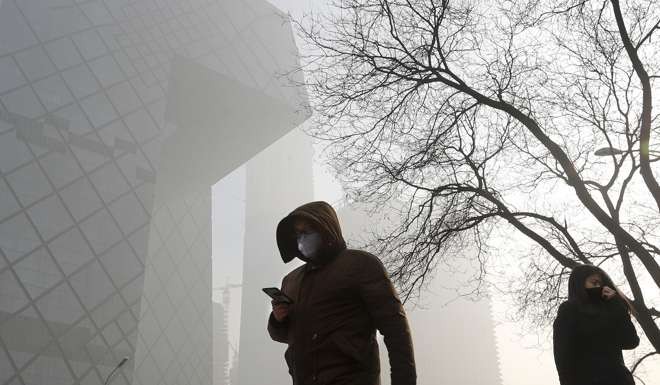 People wearing protection masks walk near the iconic headquarters of China's state broadcaster Central China Television in Beijing;s Central Business District. Photo: AP