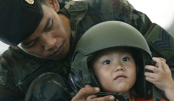 A Thai soldier helps a boy to put on a military helmet during the National Children's Day event inside a military base in Bangkok. Photo: EPA