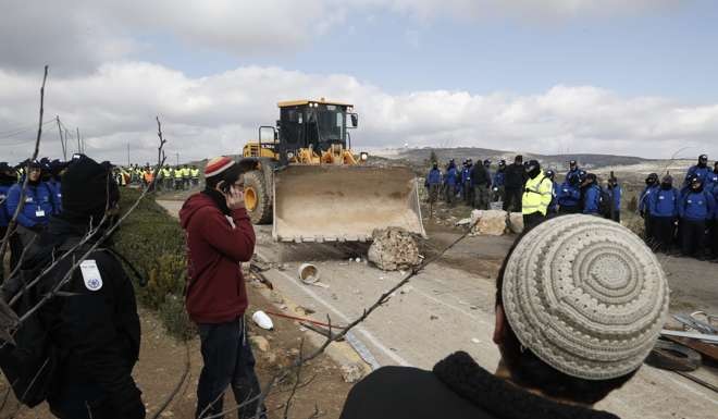 A tractor removes debris blocking a road at the Amona outpost, northeast of Ramallah. Photo: AFP