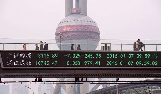 People walk along a pedestrian bridge with a screen showing stock market movements in Shanghai. Photo: AFP